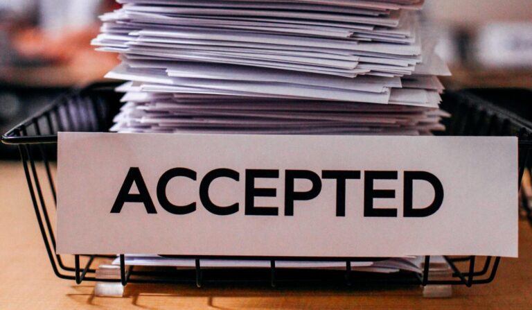 Pile of papers with 'Accepted' label in a busy office setting, highlighting information management.